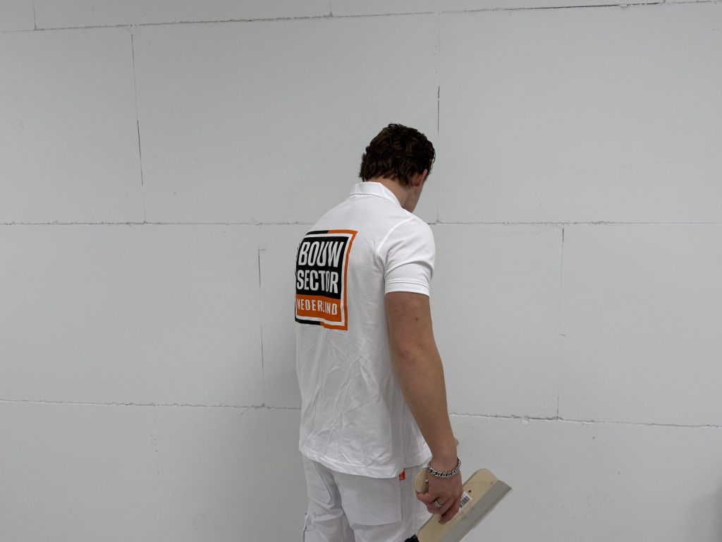 Stukadoor van Bouwsector Nederland bekijkt de ondergrond van een wand, met een spaan in de hand