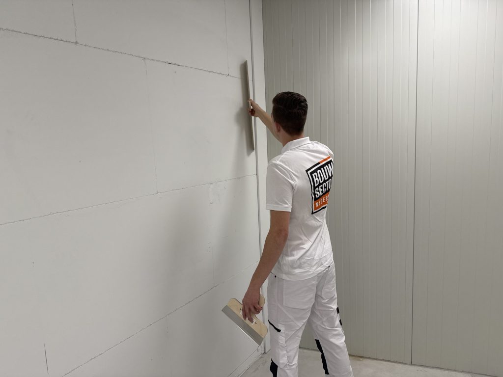 Stukadoor trekt een lange spaan verticaal langs de hoek van een wand