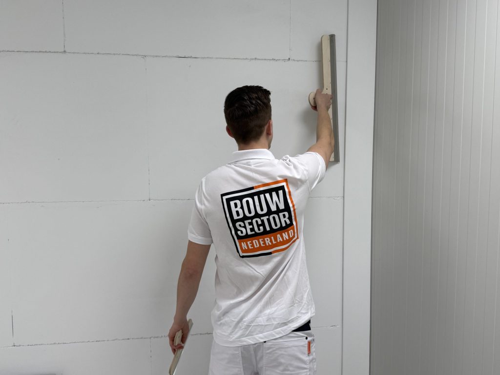Stukadoor in wit werkshirt houdt een lange spaan tegen de wand naast een binnenhoek