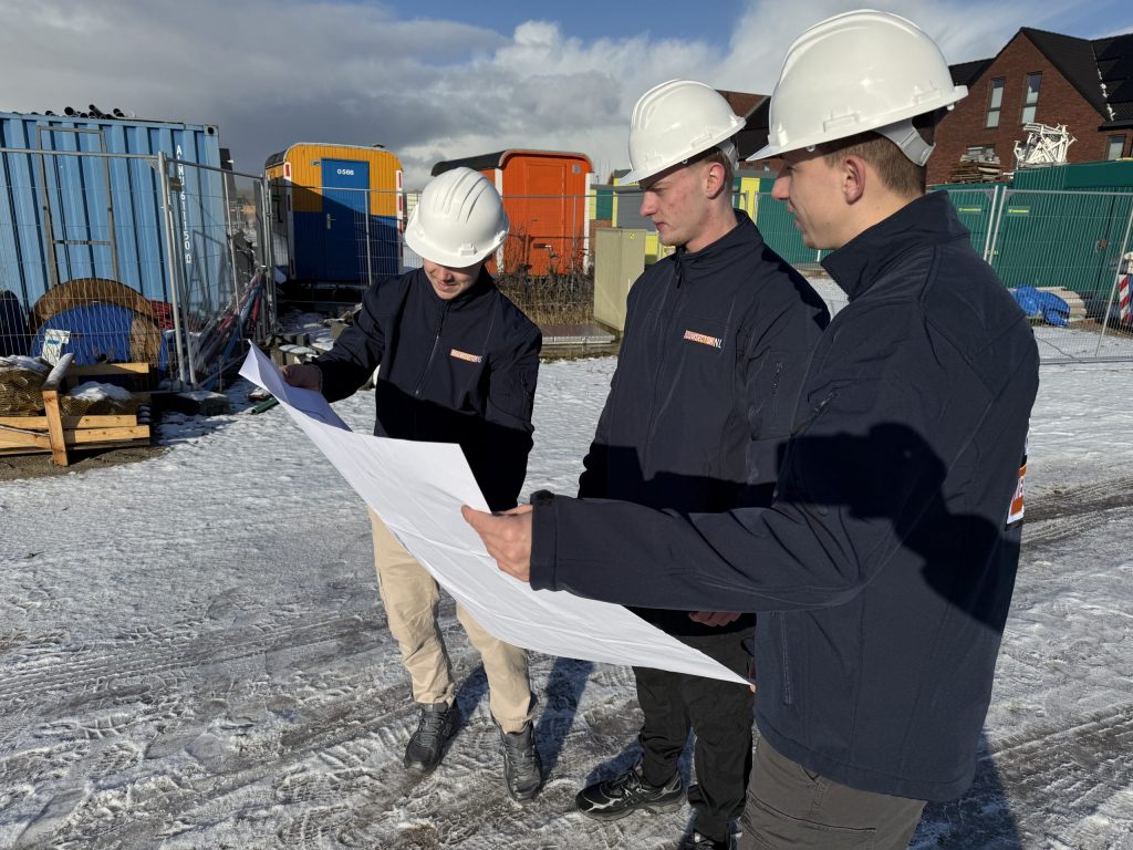 Drie vakmensen van Bouwsector Nederland met witte helm bekijken samen een bouwtekening op een bouwterrein
